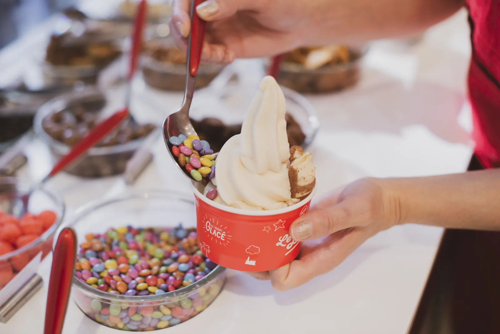 Ajout de bonbons colorés sur un pot de glace au yaourt